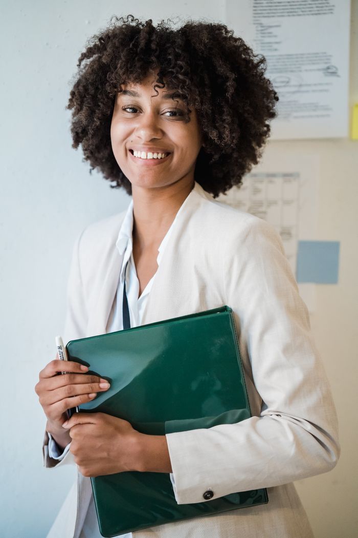 Smiling woman in business attire holding a green file in an office setting.