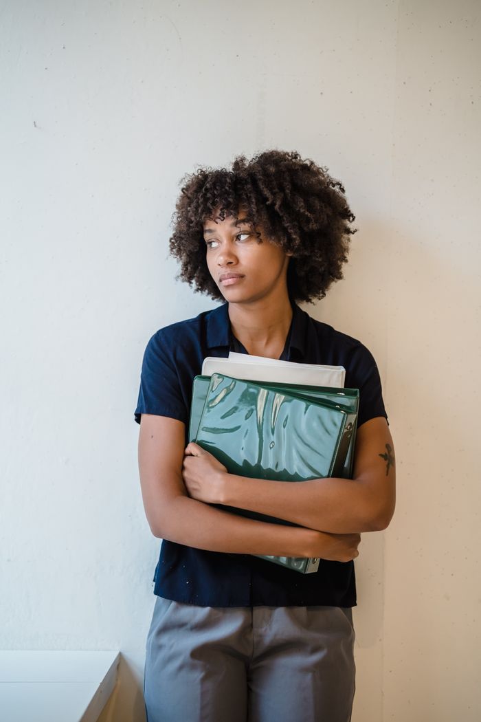 Thoughtful woman with curly hair holding green files in office setting.