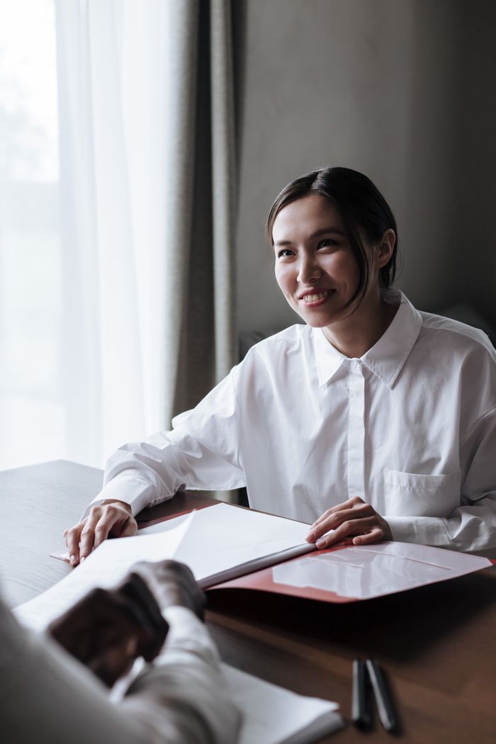 A woman in a white shirt smiles during a business meeting indoors, demonstrating professionalism and warmth.